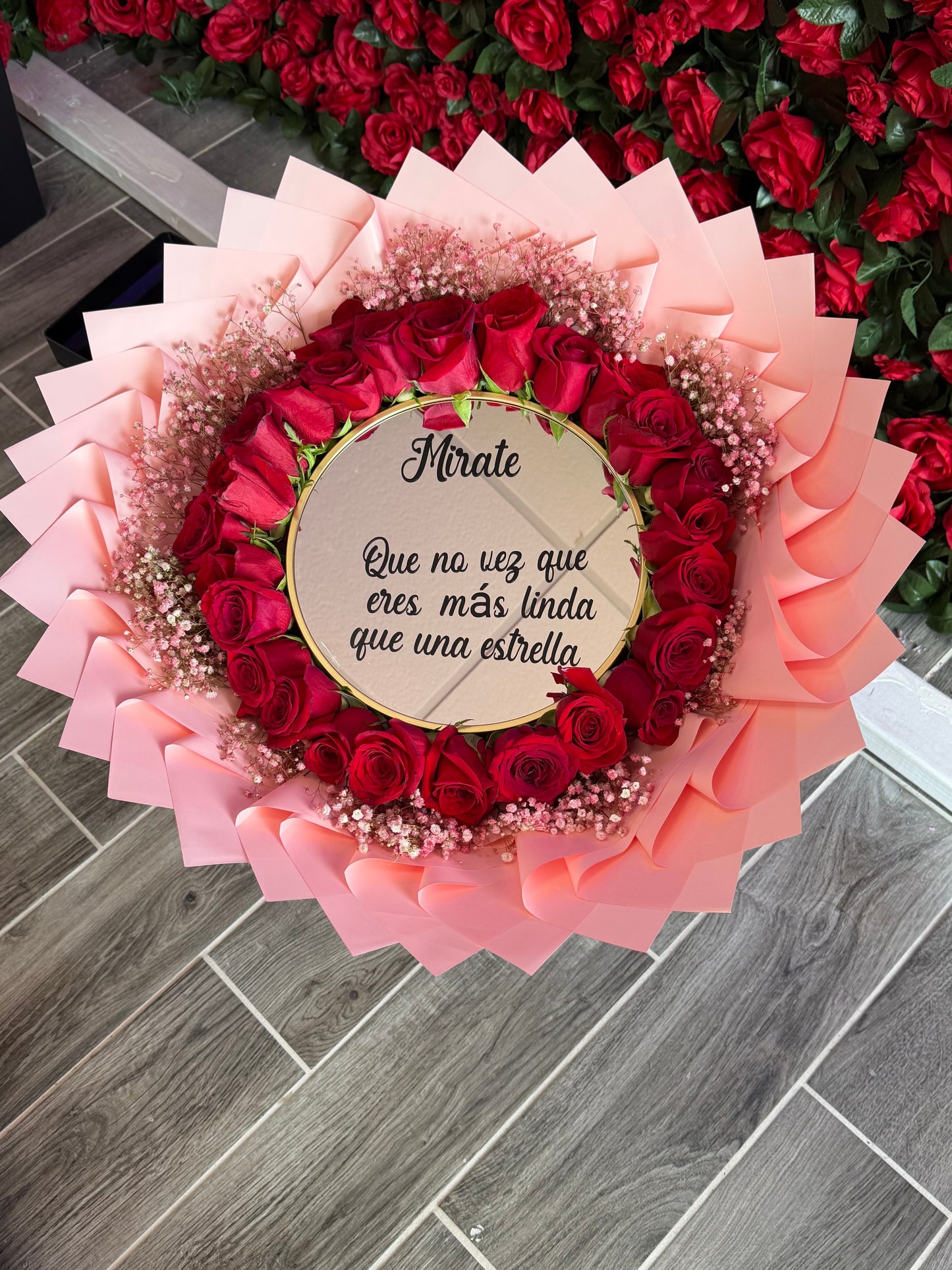 Ramo de 24 rosas rojas con un espejo en medio con la frase (Mírate ,que no vez que eres más linda que una estrella ) con baby breath alrededor pintado de rosado , con papel rosado alrededor