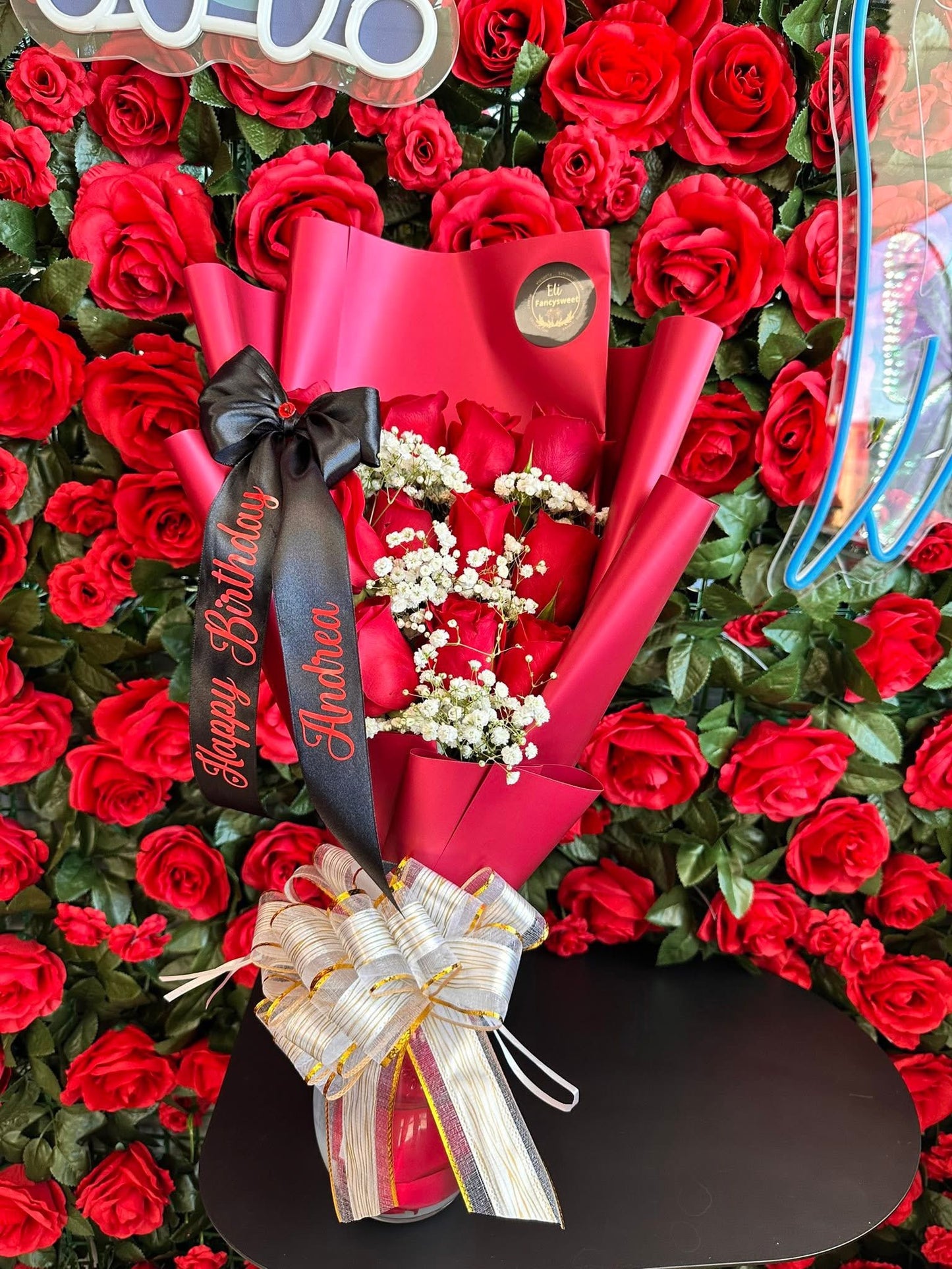 Ramo de 12 rosas rojas naturales (flat sytle) con baby breath en medio papel rojo alrededor, una frase personalizada (feliz cumpleaños Andrea )