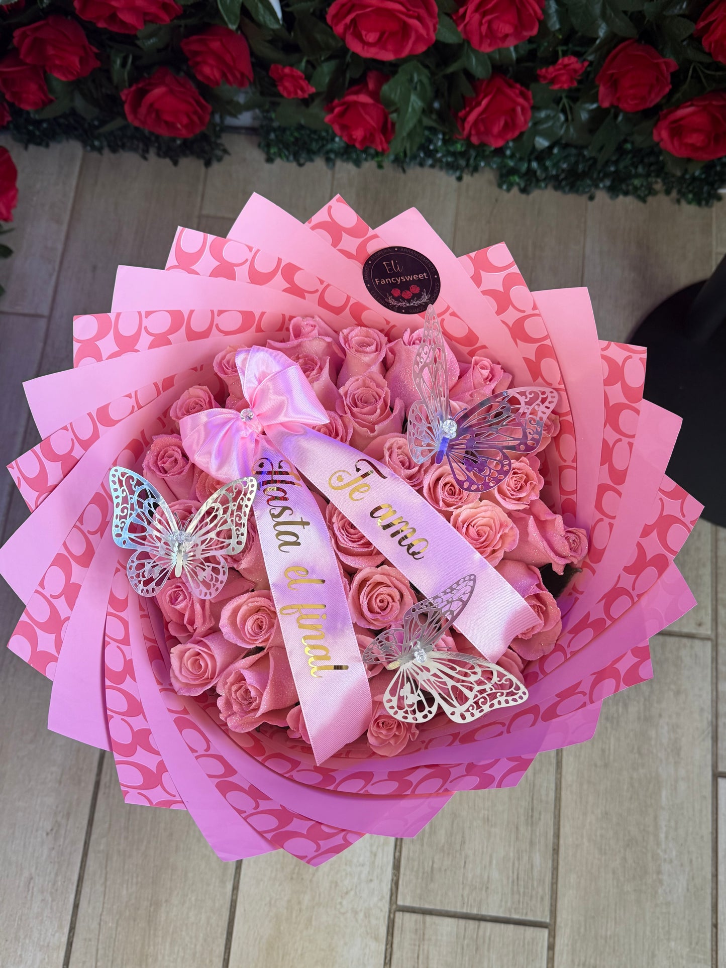 Ramo de 50 rosas rosadas con listón personalizado con papel coach rosado alrededor y 3 mariposas plateadas
