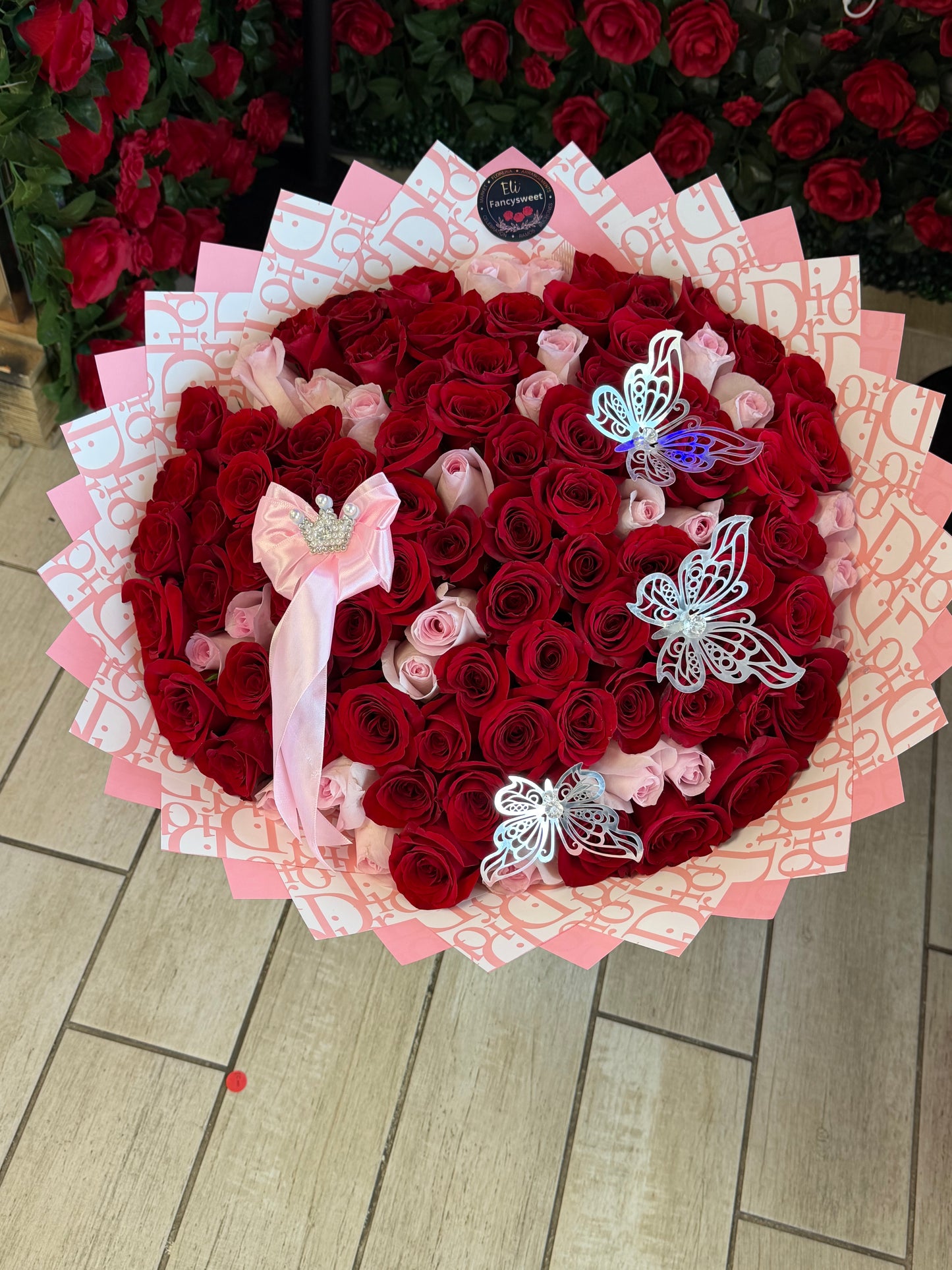 Ramo de 100 rosas rojas y rosados con papel rosado Dior alrededor un moño y 3 mariposas de decoración