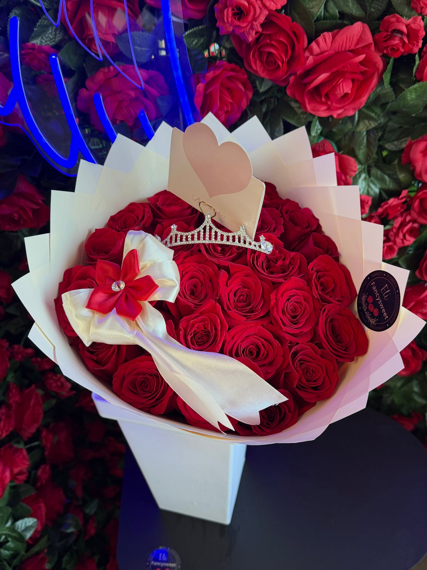 Ramo de 25 rosas rojas con papel blanco alrededor, con un moño de decoración y una mini corona