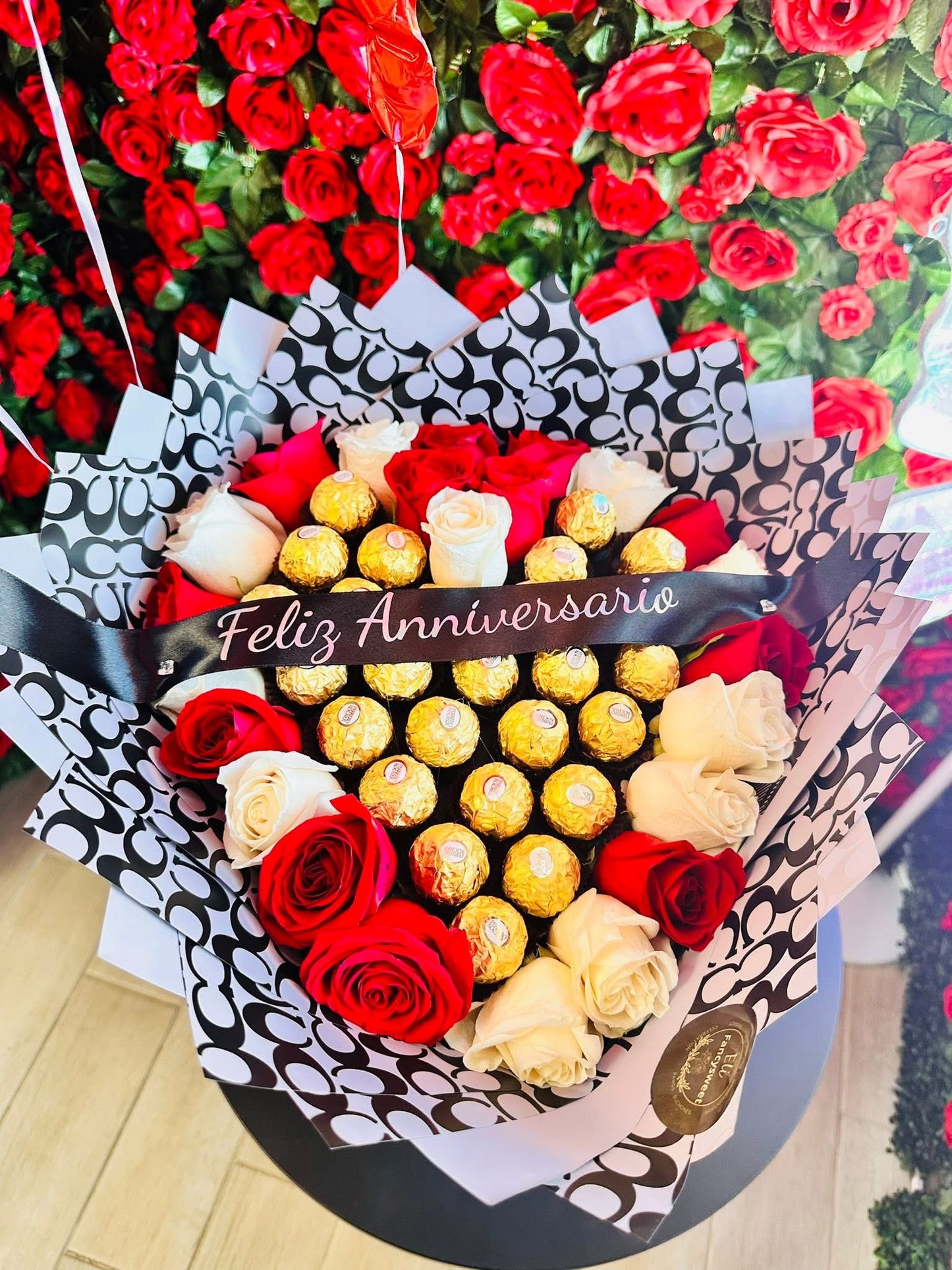 Ramo de 25 rosas rojos y blancos , con papel coach negro alrededor , con 26 chocolates Ferrero en medio y un listón personalizado en medio (Feliz aniversario)